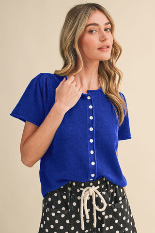 Woman wearing a blue top with white buttons and polka dot pants on a beige background