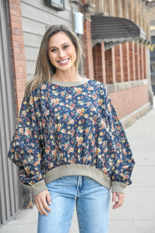 This denim washed floral balloon sleeve top is a standout piece with serious boutique energy — a rich navy floral print on a washed denim base is detailed with exposed frayed seams throughout the body and sleeves for an intentionally lived-in, one-of-a-kind feel.