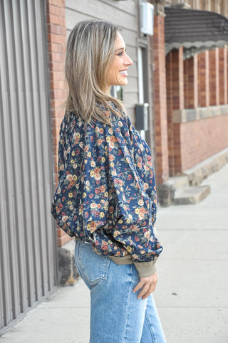 This denim washed floral balloon sleeve top is a standout piece with serious boutique energy — a rich navy floral print on a washed denim base is detailed with exposed frayed seams throughout the body and sleeves for an intentionally lived-in, one-of-a-kind feel.