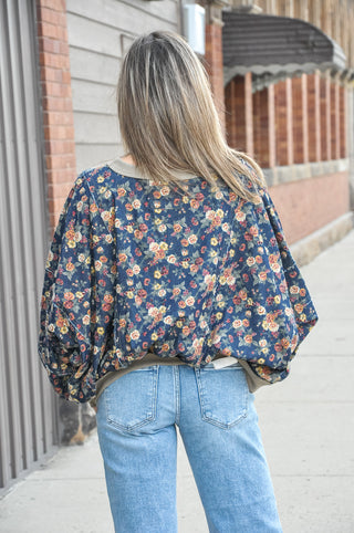 This denim washed floral balloon sleeve top is a standout piece with serious boutique energy — a rich navy floral print on a washed denim base is detailed with exposed frayed seams throughout the body and sleeves for an intentionally lived-in, one-of-a-kind feel.