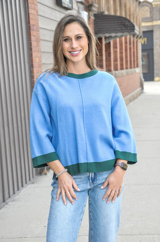 The soft blue body contrasts beautifully against forest green ribbed trim at the crew neckline, cuffs, and hem for a polished, sporty-chic look. 