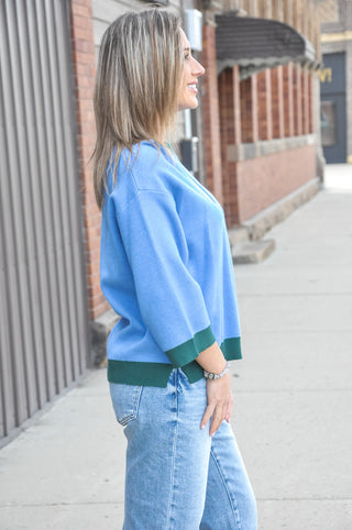 The soft blue body contrasts beautifully against forest green ribbed trim at the crew neckline, cuffs, and hem for a polished, sporty-chic look. 