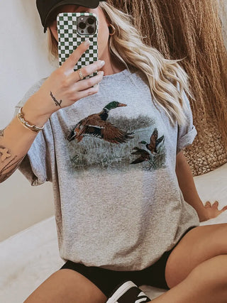 Person wearing a gray t-shirt with a duck design, holding a phone with a checkered case.