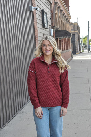 This burgundy quilted sweatshirt features a mock half button neckline and plaid contrast trim for a look that's equal parts cozy and put-together. 