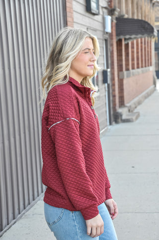 This burgundy quilted sweatshirt features a mock half button neckline and plaid contrast trim for a look that's equal parts cozy and put-together. 