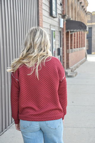 This burgundy quilted sweatshirt features a mock half button neckline and plaid contrast trim for a look that's equal parts cozy and put-together. 